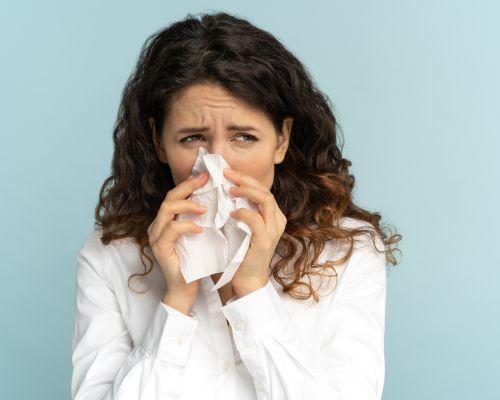 A woman problem for Allergic Rhinitis and using a tissue to blow her nose.